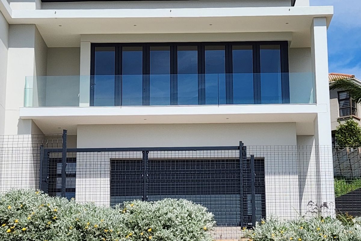 Modern rear elevation featuring a spacious balcony with glass balustrades, large folding glass doors, and a secure ground-level garage area.