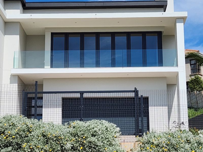 Modern rear elevation featuring a spacious balcony with glass balustrades, large folding glass doors, and a secure ground-level garage area.