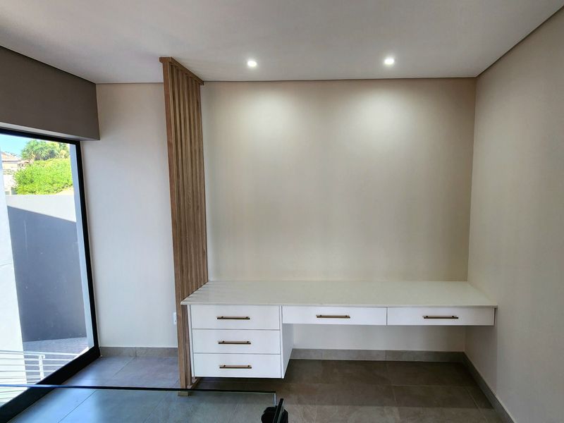 A modern, minimalist home office space featuring a sleek built-in desk with integrated drawers and a decorative timber slat partition.