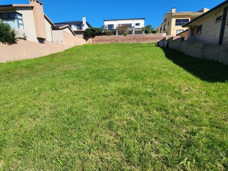 A sloped residential vacant plot featuring established boundary walls and a rear retaining wall, offering a clear space for future development.