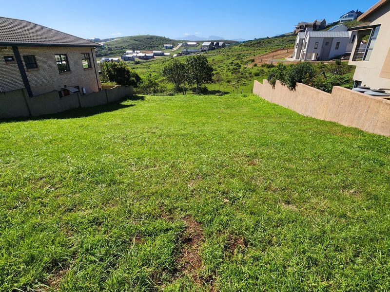 A vacant residential plot featuring a gentle slope, enclosed by boundary walls, and offering scenic views of the surrounding neighborhood and hills.