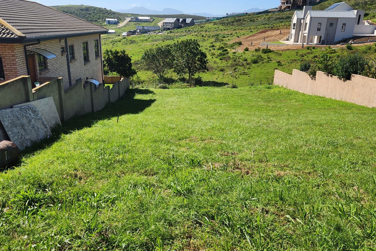 A vacant residential plot featuring a gentle slope, enclosed by boundary walls, situated in a developing neighborhood with scenic hillside views.