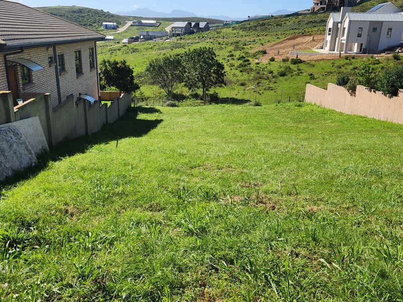 A vacant residential plot featuring a gentle slope, enclosed by boundary walls, situated in a developing neighborhood with scenic hillside views.