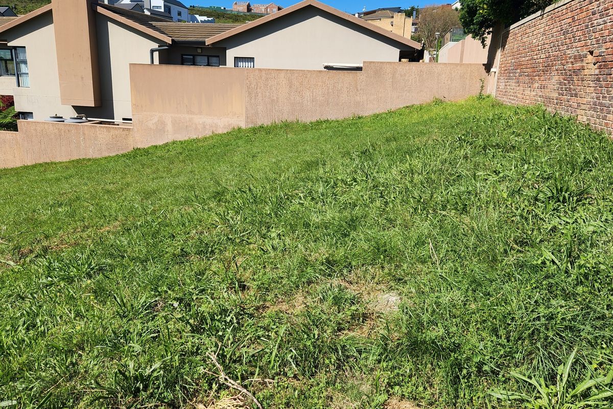 A sloped residential plot featuring established boundary walls and surrounding residential development.