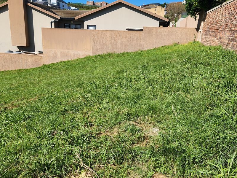 A sloped residential plot featuring established boundary walls and surrounding residential development.