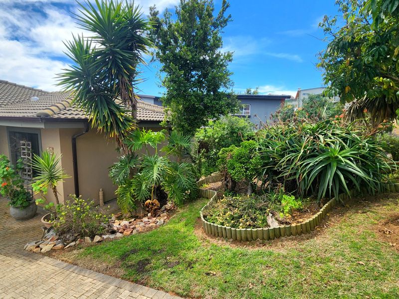 Front exterior view of the house featuring a paved driveway, tiled roof, and established garden with mature plantings and timber edging.
