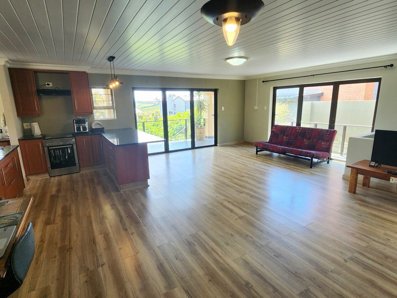 Spacious open-plan living area featuring a modern kitchen with timber cabinetry, granite countertops, and large sliding doors leading to an outdoor balcony.