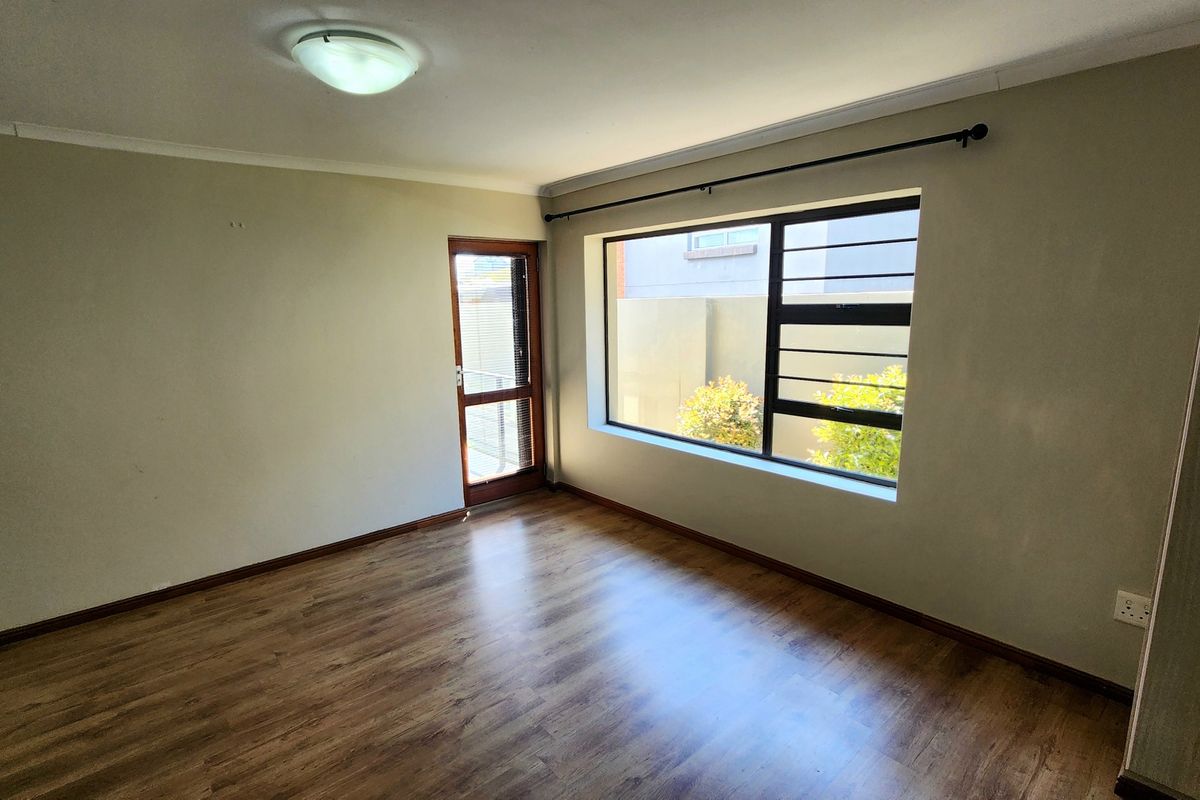 A bright, empty bedroom featuring laminate flooring, a built-in cupboard, and large windows with security bars, offering a clean and neutral living space.