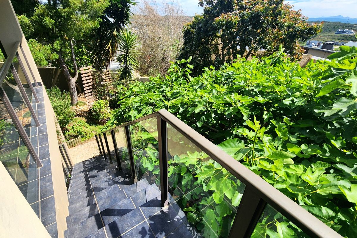 An outdoor tiled staircase with a modern glass balustrade leading down into a lush, well-maintained garden area.