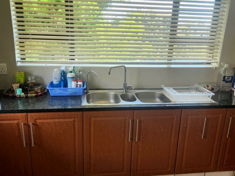 A functional kitchen area featuring a double bowl stainless steel sink, granite countertops, and wood-finish cabinetry with integrated storage.