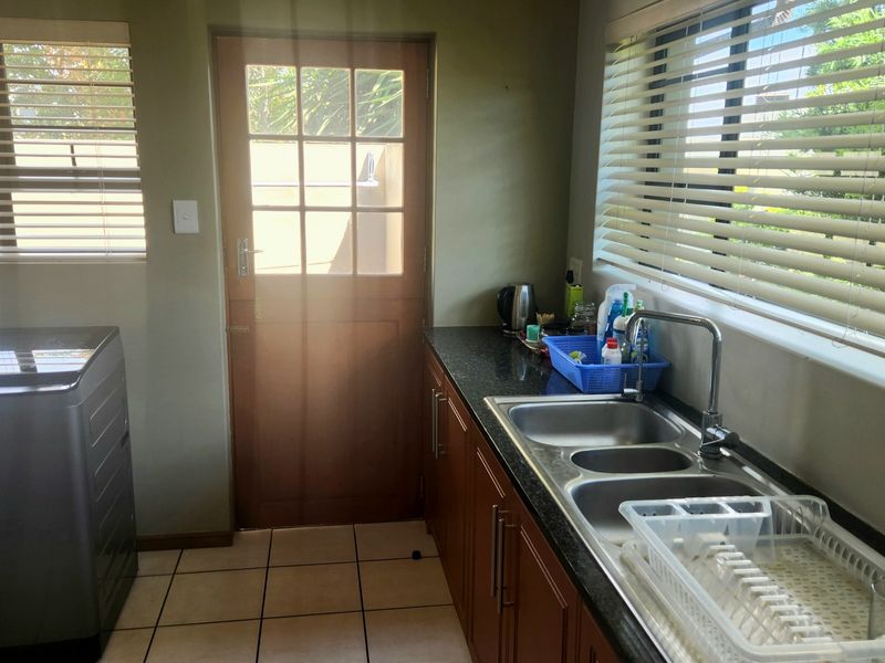 A functional laundry room featuring granite countertops, double stainless steel sink, wooden cabinetry, and direct access to the exterior via a timber door.