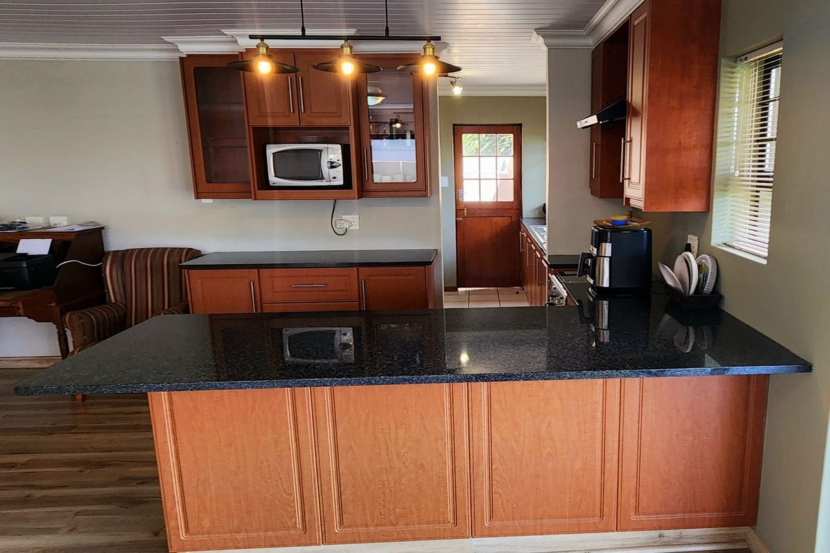 A functional kitchen featuring wooden cabinetry, granite countertops, and a breakfast bar, with a connecting door leading to an adjacent utility area.