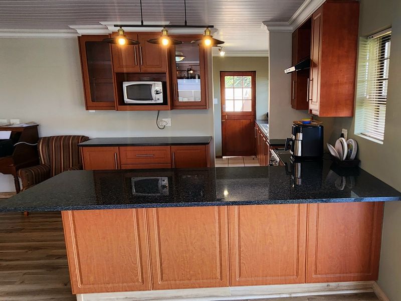A functional kitchen featuring wooden cabinetry, granite countertops, and a breakfast bar, with a connecting door leading to an adjacent utility area.
