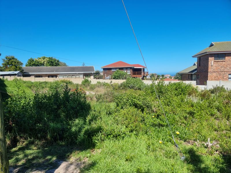 A vacant residential plot featuring overgrown vegetation and a boundary wall, situated in a developed neighborhood with surrounding houses.
