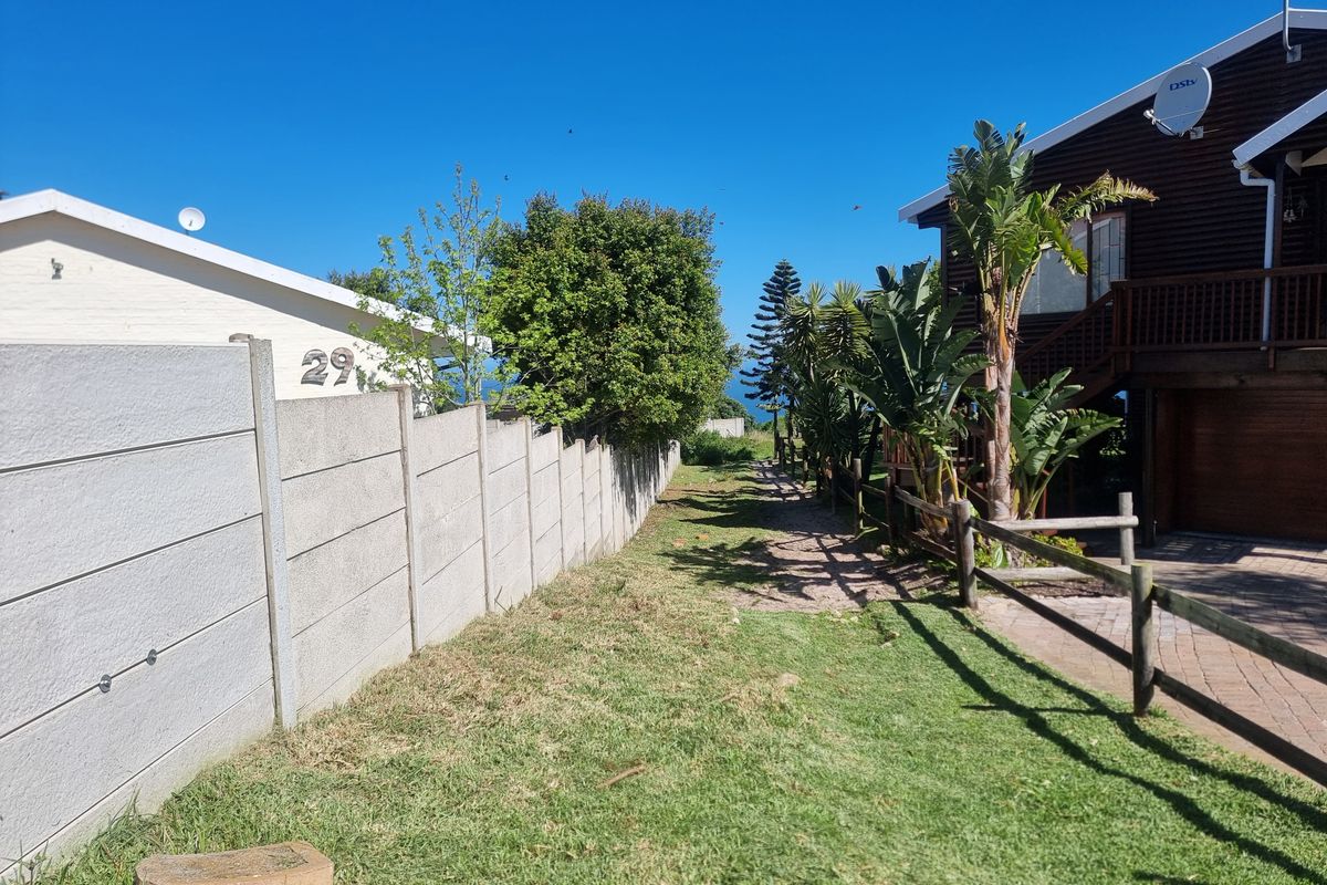 A view of the rear exterior area featuring a precast concrete boundary wall, timber fencing, and a paved driveway leading to the property.