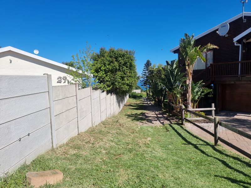 A view of the rear exterior area featuring a precast concrete boundary wall, timber fencing, and a paved driveway leading to the property.