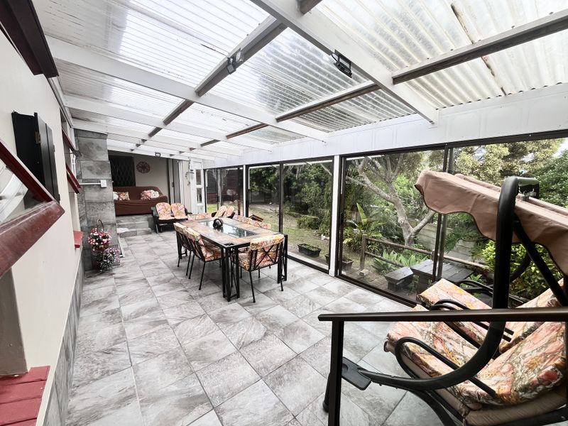 A covered patio area featuring tiled flooring, a corrugated roof, and large sliding glass doors overlooking the garden.