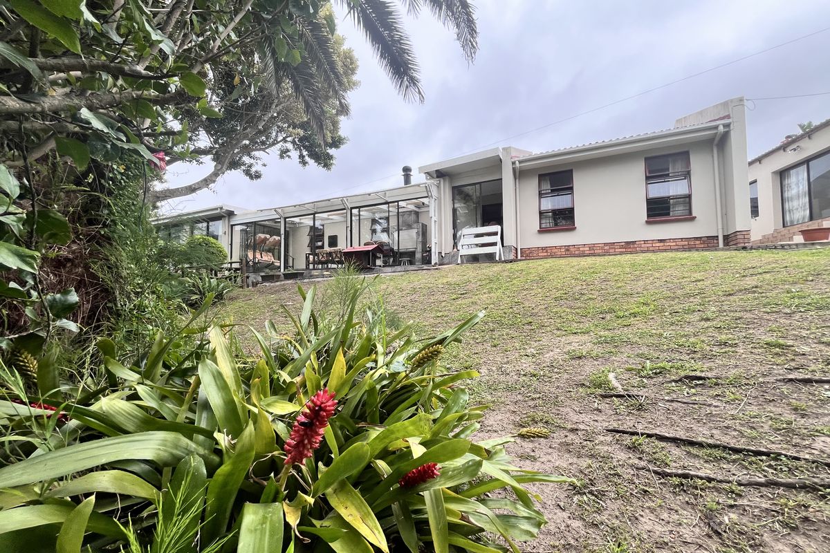 Rear view of the house featuring an enclosed patio area, brick foundation, and a spacious garden with established trees.