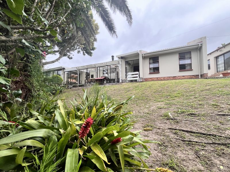 Rear view of the house featuring an enclosed patio area, brick foundation, and a spacious garden with established trees.