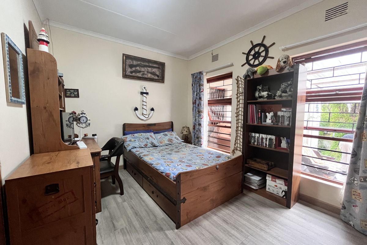 A well-maintained bedroom featuring laminate flooring, coving, and large windows fitted with security burglar bars.