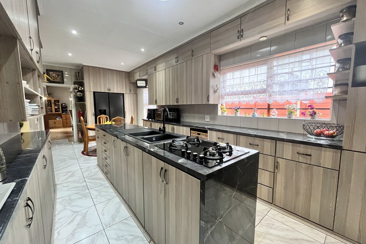 Modern kitchen featuring wood-grain cabinetry, dark stone countertops, a central island with a gas hob, and marble-look tiled flooring.
