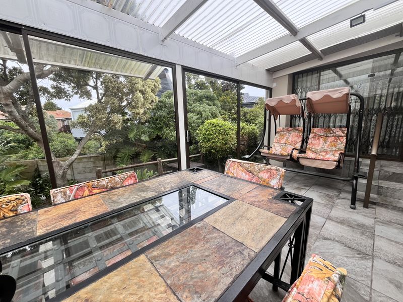Enclosed patio area featuring a corrugated roof, tiled flooring, and large sliding glass doors overlooking the garden.