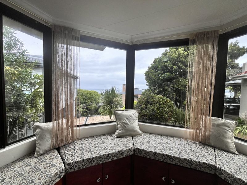 A cozy corner window seat featuring built-in cabinetry and expansive views of the surrounding garden and distant sea.