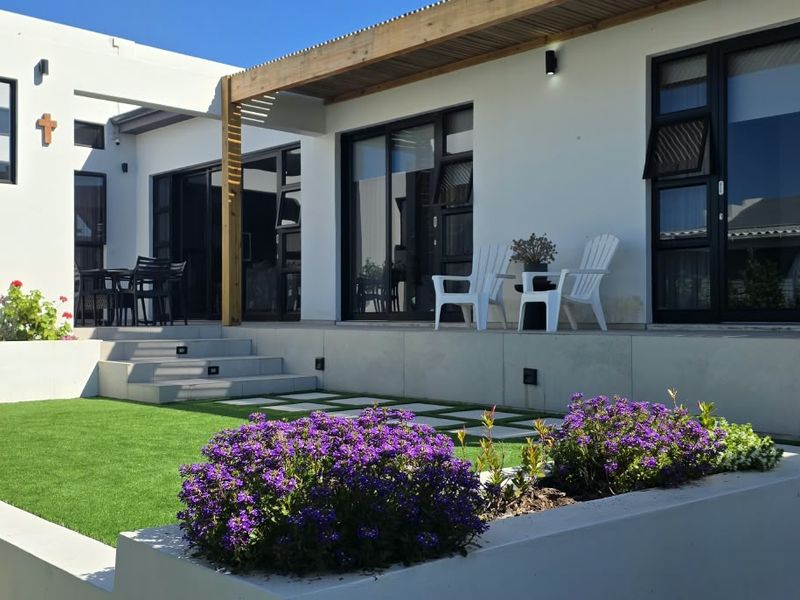 Modern rear exterior featuring a landscaped garden with artificial lawn, stepped patio area, timber pergola, and large sliding glass doors.