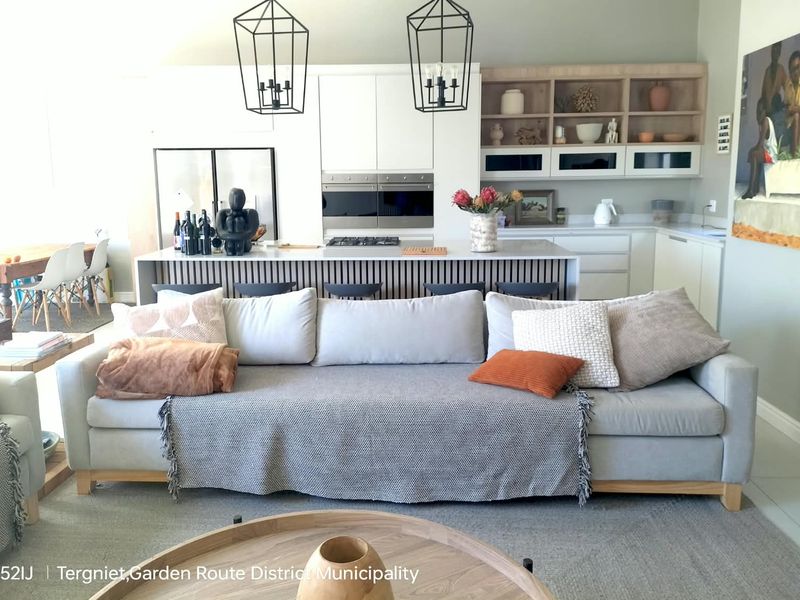 Modern open-plan living area featuring a contemporary kitchen with a central island, built-in appliances, and stylish pendant lighting, seamlessly integrated with the lounge space.