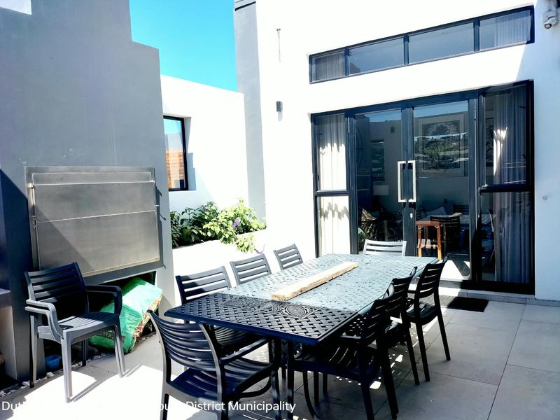 A modern covered patio featuring a built-in stainless steel braai, tiled flooring, and large aluminium sliding doors providing seamless access to the interior living space.