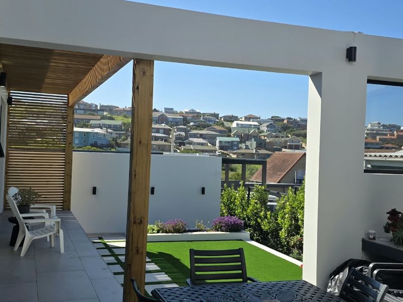 A modern covered patio featuring tiled flooring, timber ceiling accents, and a built-in planter box, overlooking a residential neighborhood.