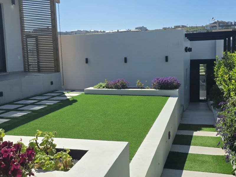 A well-maintained rear garden featuring artificial turf, raised concrete planters, a paved walkway, and modern wall-mounted lighting, providing a clean outdoor living space.