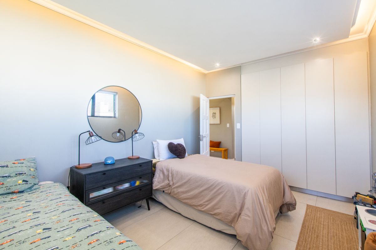 A well-maintained bedroom featuring neutral tiled flooring, extensive built-in cupboards, and modern recessed cove lighting.