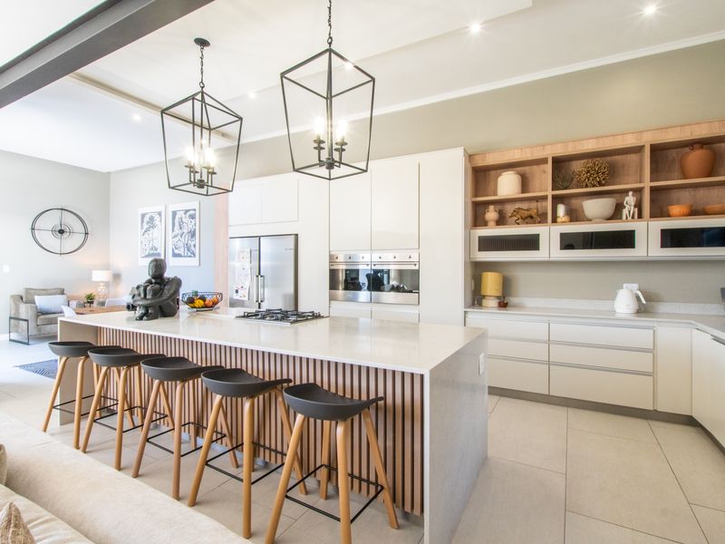 Modern open-plan kitchen featuring a large island with stone countertops, integrated appliances, sleek cabinetry, and stylish pendant lighting, seamlessly flowing into the living area.