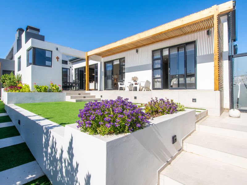 Modern rear exterior featuring a timber pergola, tiered artificial lawn, raised garden beds, and large sliding glass doors leading into the home.