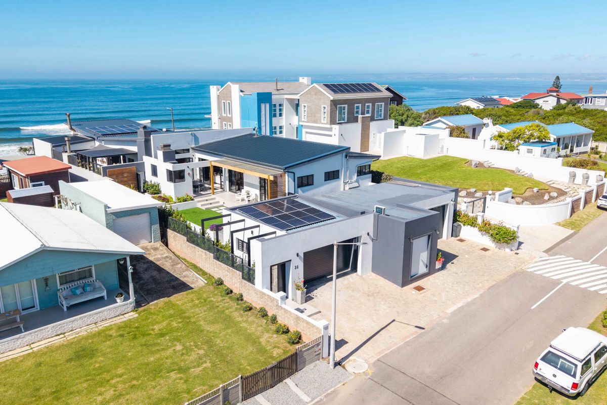 Aerial view of a modern coastal property featuring solar panels, a paved driveway, and a garage, situated near the ocean.