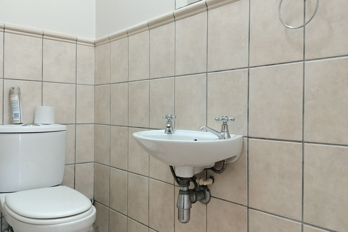 A functional guest bathroom featuring a wall-mounted basin and a close-coupled toilet, finished with neutral ceramic wall tiles.