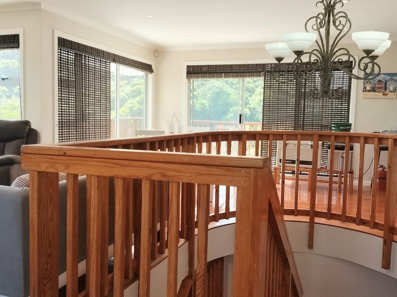 Open plan living area featuring hardwood flooring, a prominent wooden balustrade, and sliding glass doors that provide natural light and access to the outdoors.