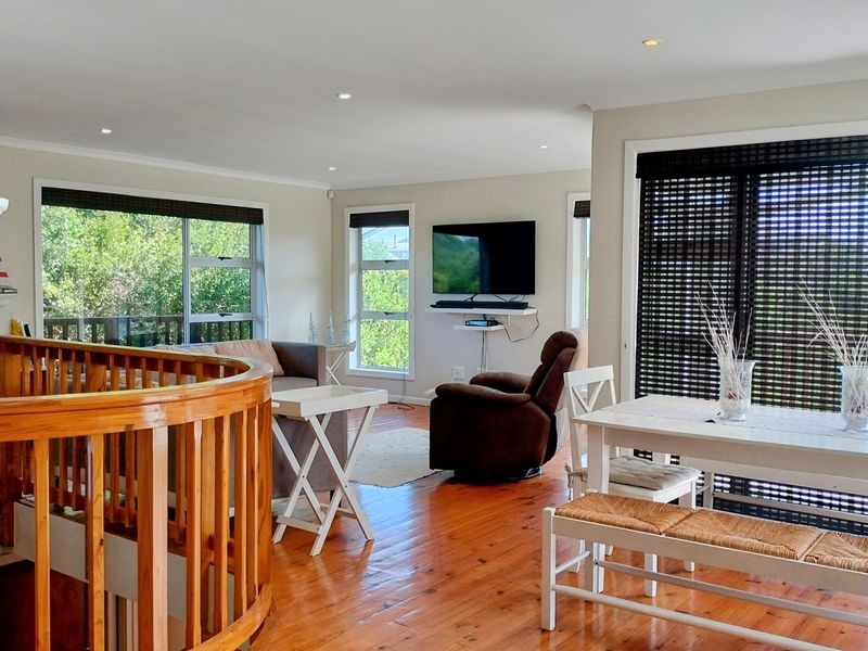 Spacious open-plan living and dining area featuring polished timber flooring, a decorative wooden balustrade, and large windows providing ample natural light.