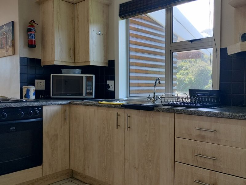A functional kitchen featuring light wood-finish cabinetry, dark tiled backsplash, granite-look laminate countertops, and a built-in oven with hob.