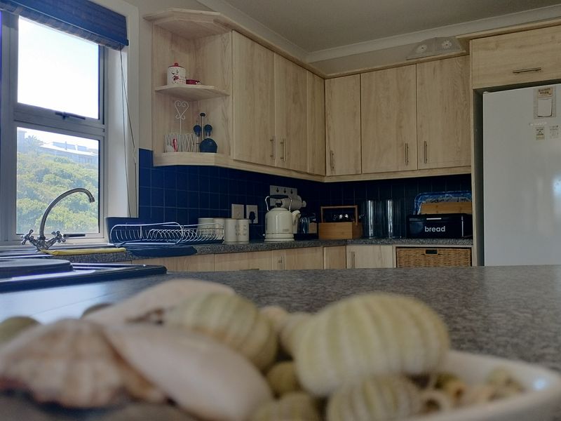 A functional kitchen featuring light wood-tone cabinetry, dark tiled backsplash, and ample countertop space with a view through the window.