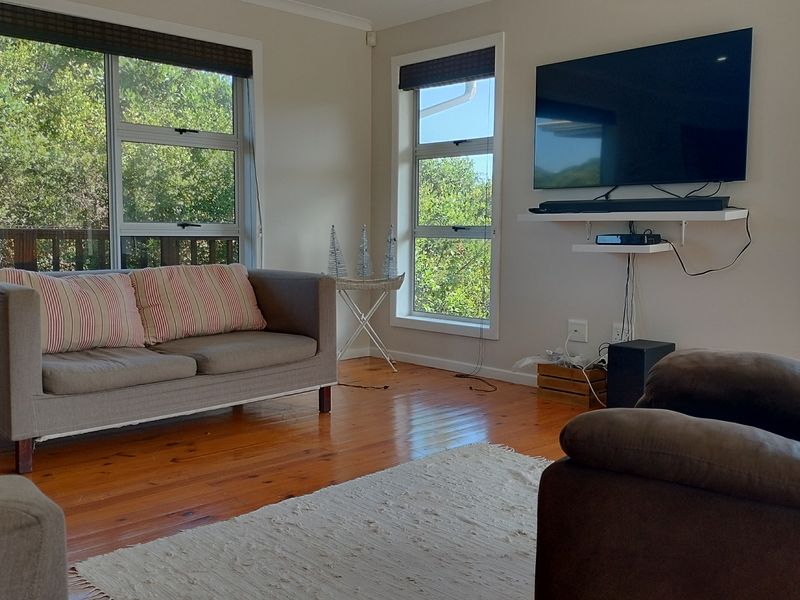 A bright living room featuring polished timber flooring and large windows that provide ample natural light and views of the surrounding greenery.
