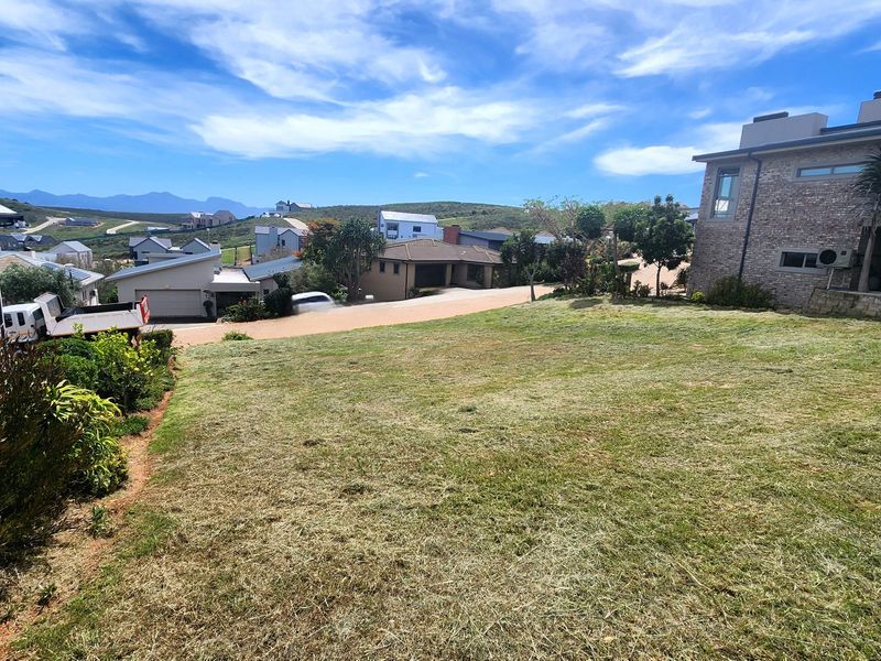 A view of a sloped residential plot with established lawn, adjacent to neighboring properties in a developed estate setting.