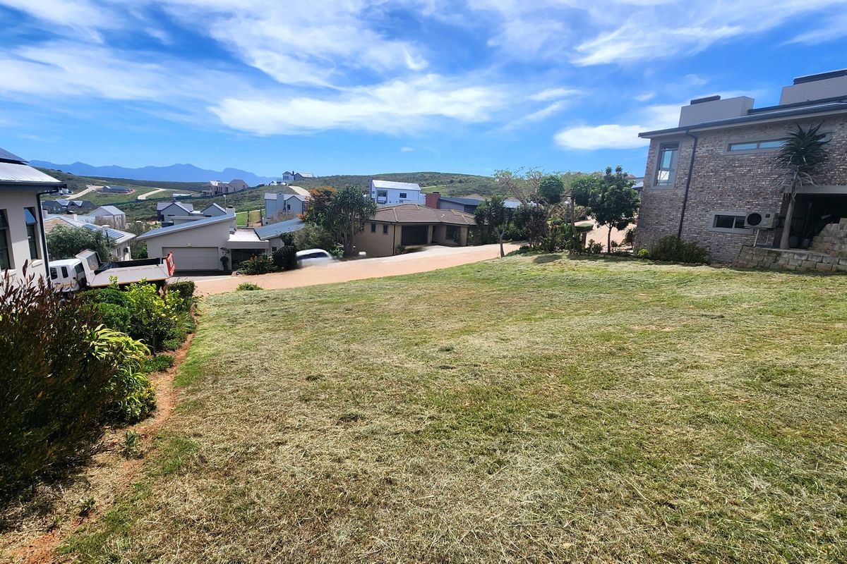 A view of a sloped residential plot with established lawn, adjacent to neighboring properties in a developed estate setting.