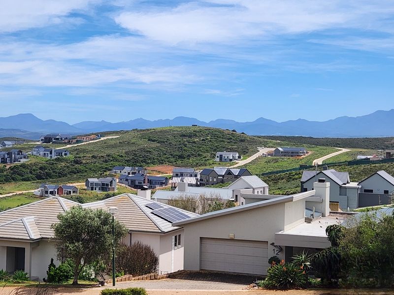 An elevated view of a residential estate featuring modern homes with tiled roofs, solar panels, and scenic mountain landscape in the background.
