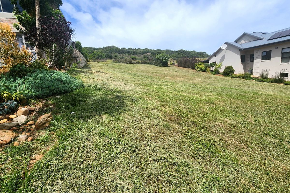 A spacious, well-maintained residential garden area featuring a gentle slope, established landscaping, and a stone retaining wall adjacent to neighboring properties.