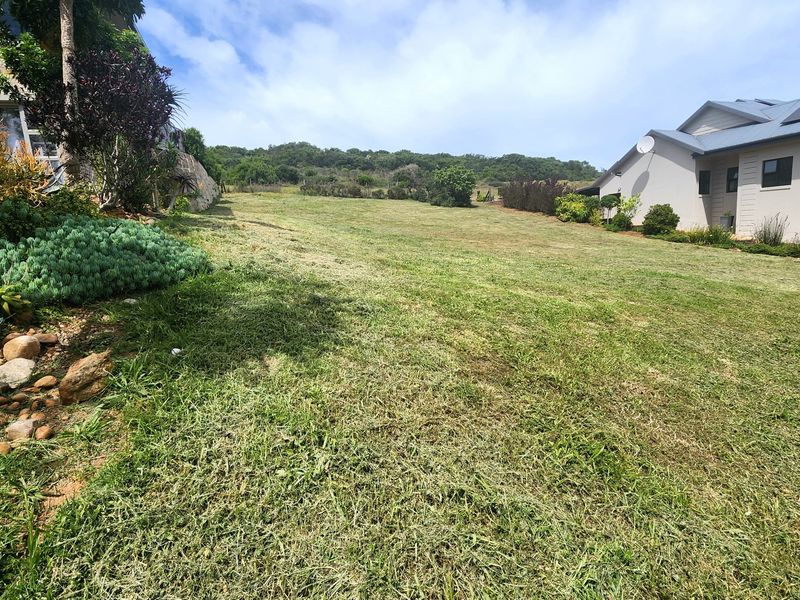 A spacious, well-maintained residential garden area featuring a gentle slope, established landscaping, and a stone retaining wall adjacent to neighboring properties.