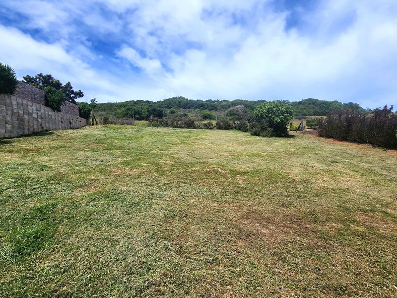 A spacious, well-maintained residential vacant plot featuring a stone retaining wall and established perimeter landscaping.