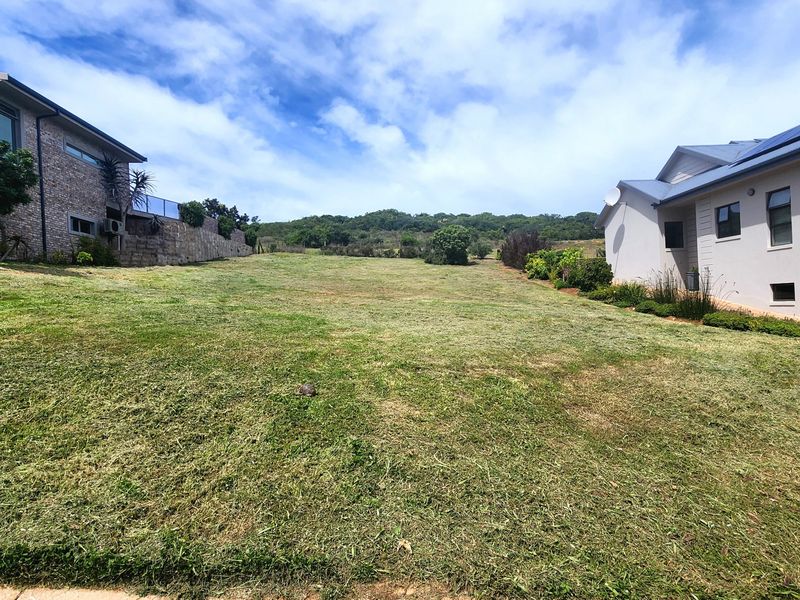 A vacant residential plot situated between two existing modern homes, featuring a well-maintained grass lawn and established retaining wall.