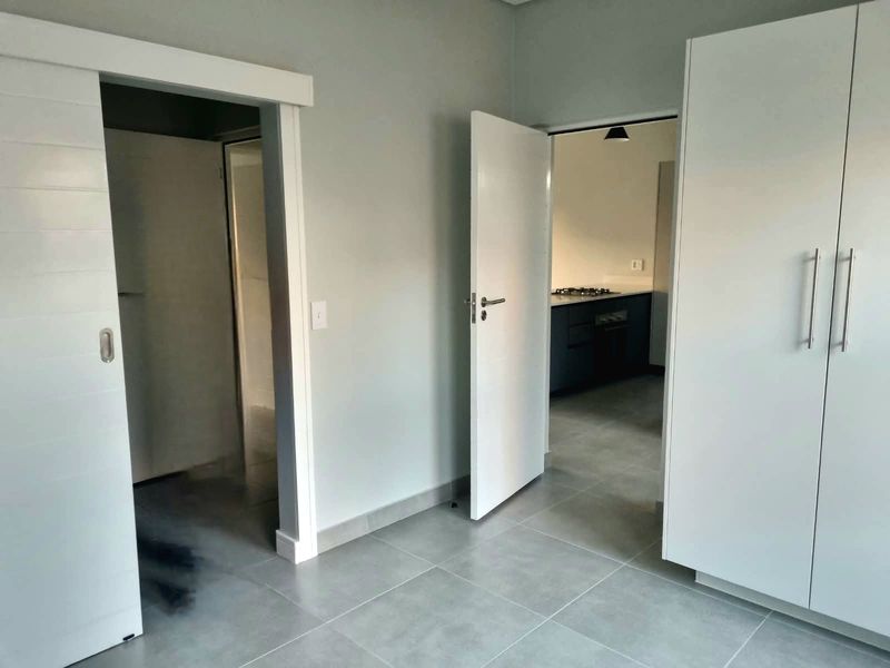 A clean, modern hallway featuring neutral tiled flooring, built-in storage cupboards, and access to adjacent rooms including a kitchen area.